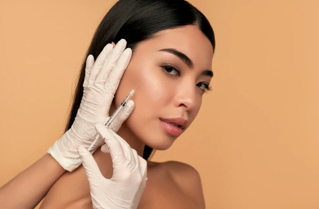 A professional wearing white gloves carefully administers an injection near a woman's cheek, representing radiesse and sculptra treatments designed to restore facial volume, enhance skin elasticity, and improve overall contour for a youthful and rejuvenated appearance.